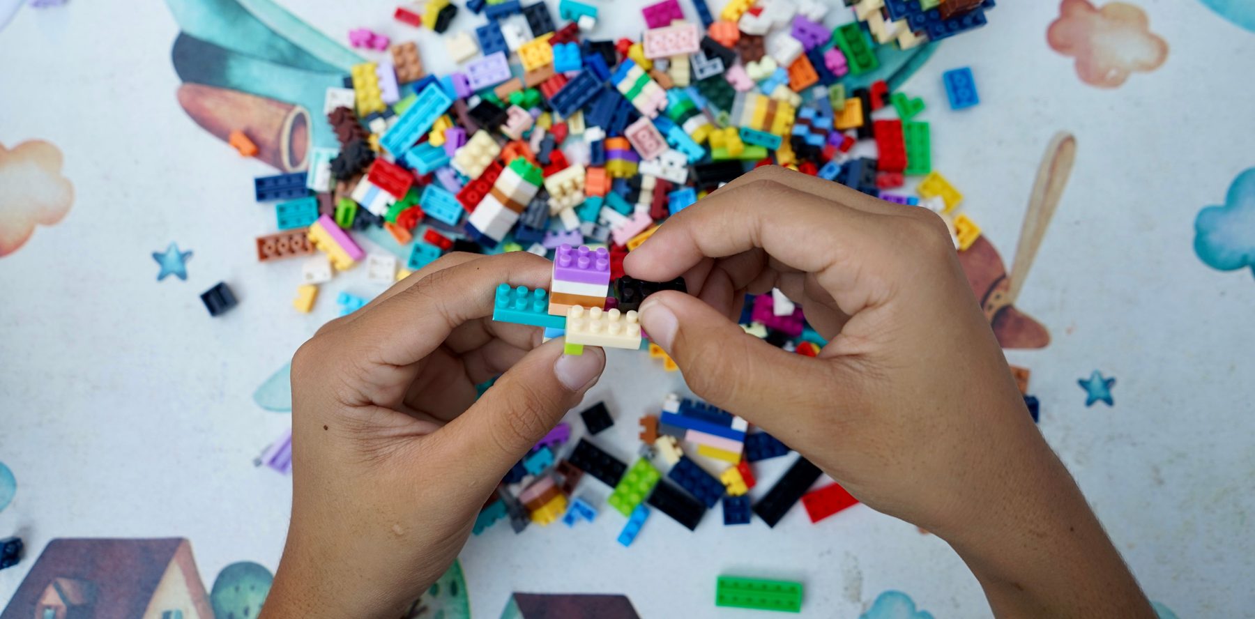 Twee handen die een paar LEGO-steentjes aan elkaar klikken boven een berg losse steentjes