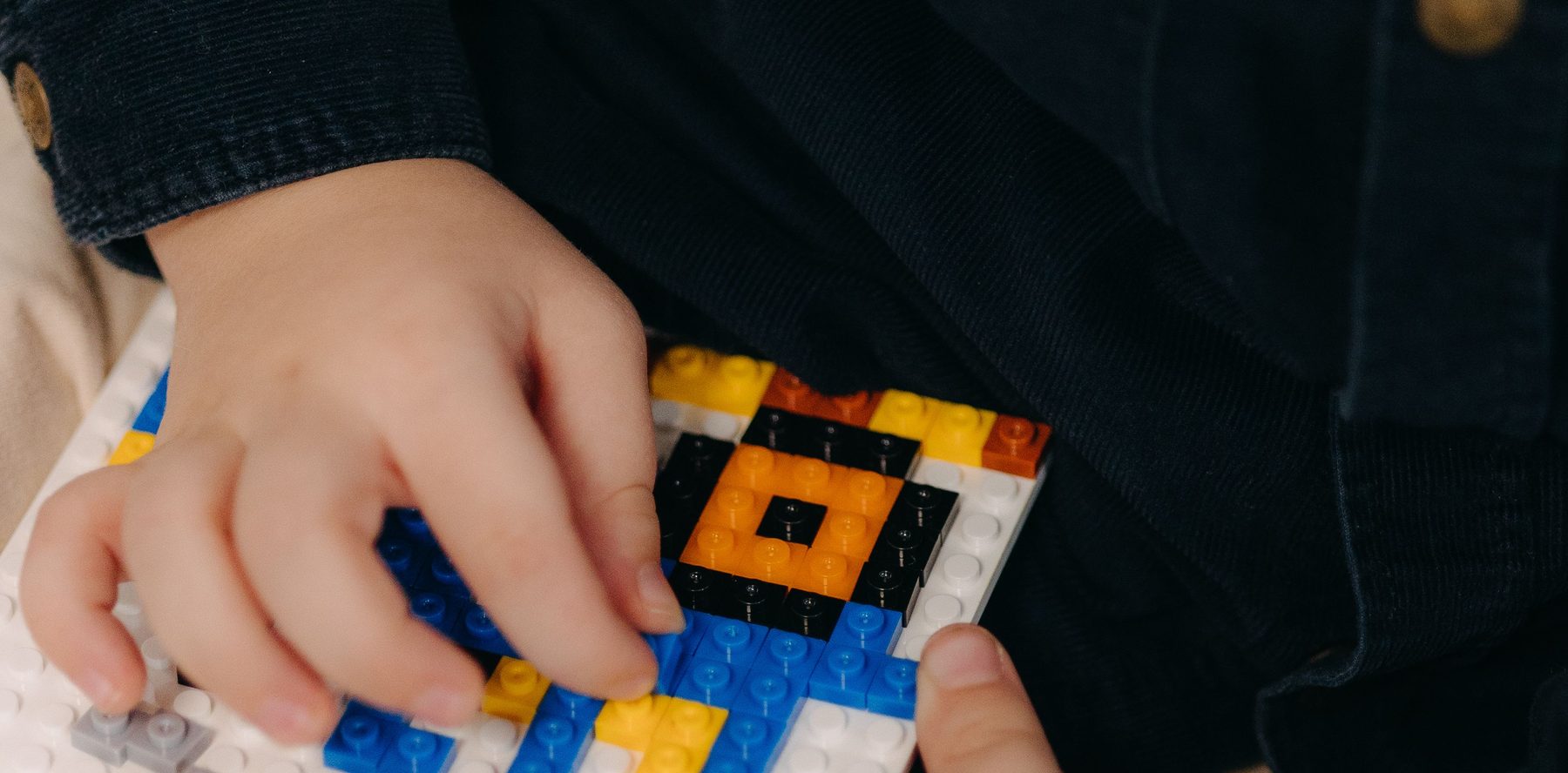 Een kinderhand die gekleurde steentjes op een witte bouwplaat drukt