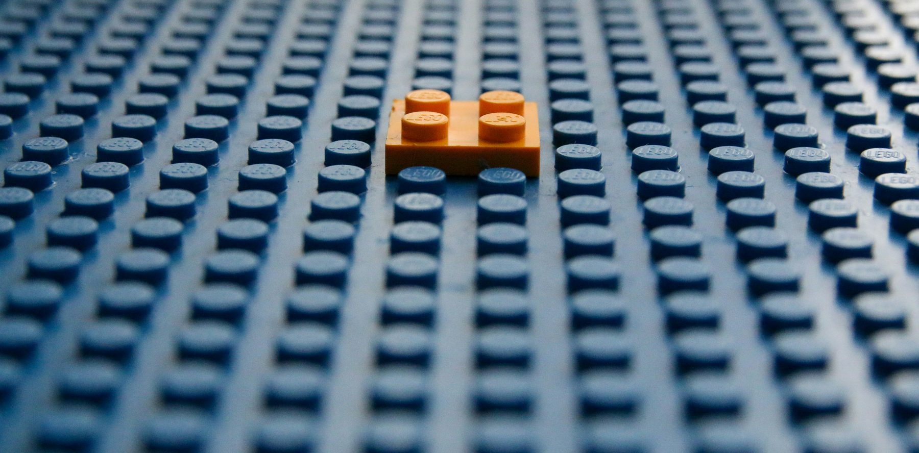 Eén oranje steentje op een blauwe LEGO-bouwplaat