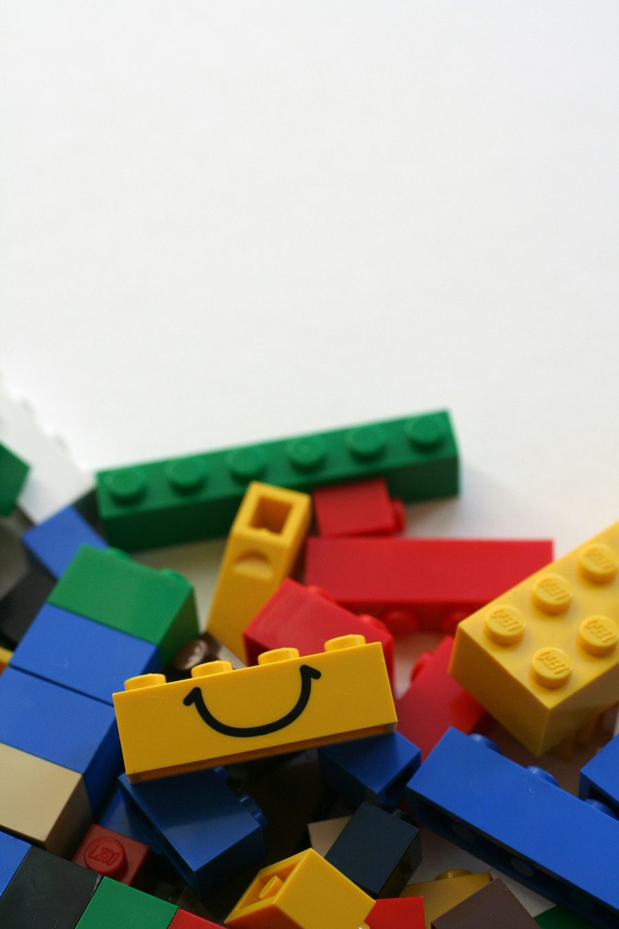 Een geel LEGO-steentje met een lachend gezichtje, tussen losse steentjes